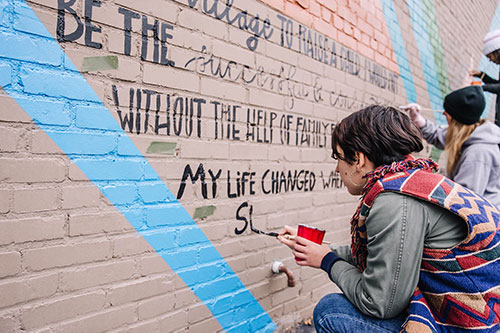 A few folks painting stories of fulfilled needs on the Giving Wall mural at Perch