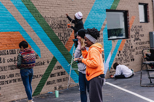 A few folks laughing while painting the Giving Wall mural at Perch